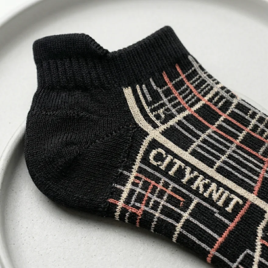 Close-up of a custom black ankle sock with a cream and coral city-map pattern and a woven CITYKNIT logo