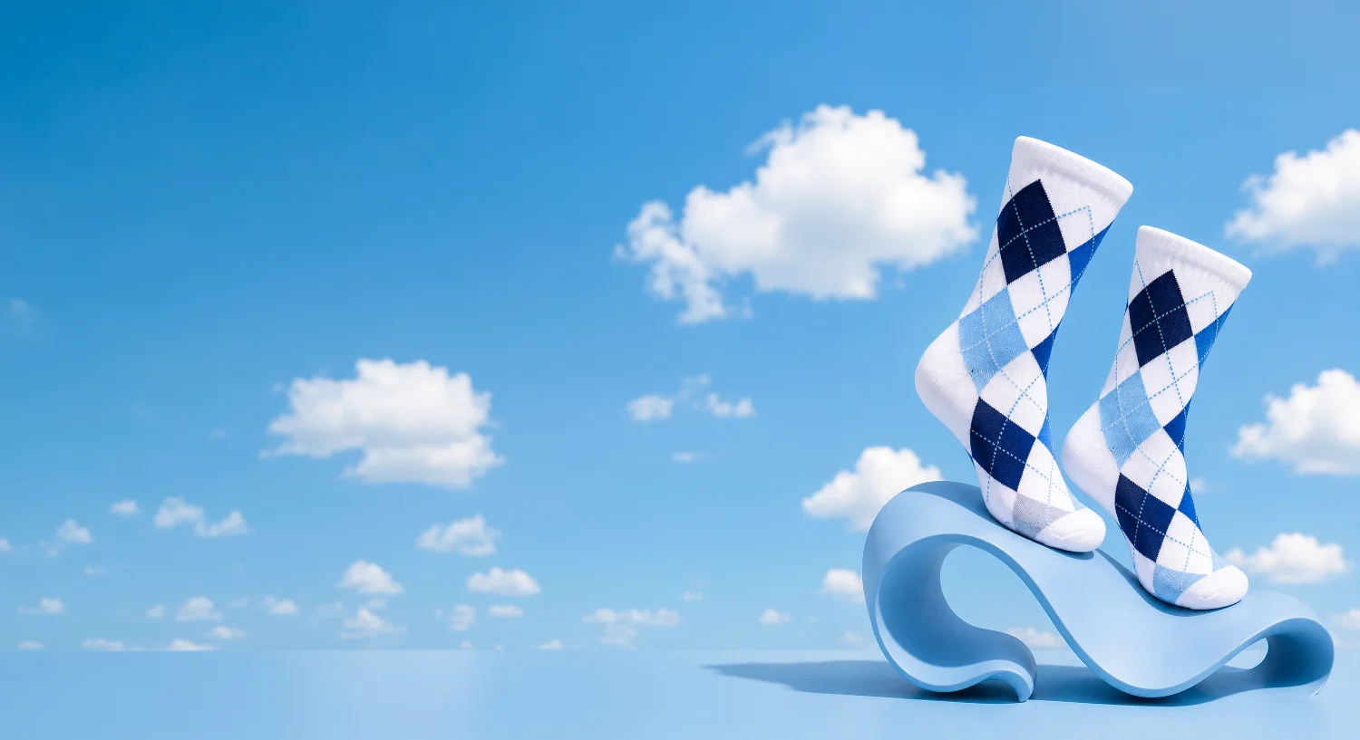 Custom blue and white argyle socks balanced on a sculptural wave against a bright blue sky with clouds
