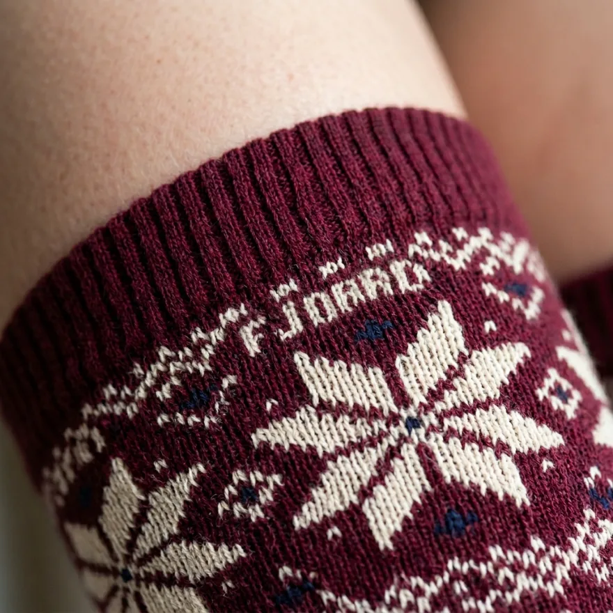Close-up of custom burgundy high-knee socks with a cream Fair Isle snowflake pattern and a woven FJORD logo