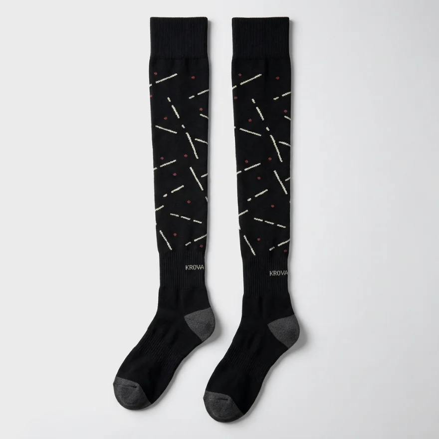 A pair of custom black high-knee socks with a cream and red track-mark pattern and a woven KROVA logo