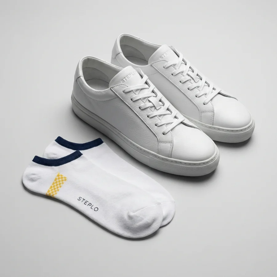 Custom white no-show socks with a navy cuff and yellow accent beside white leather sneakers
